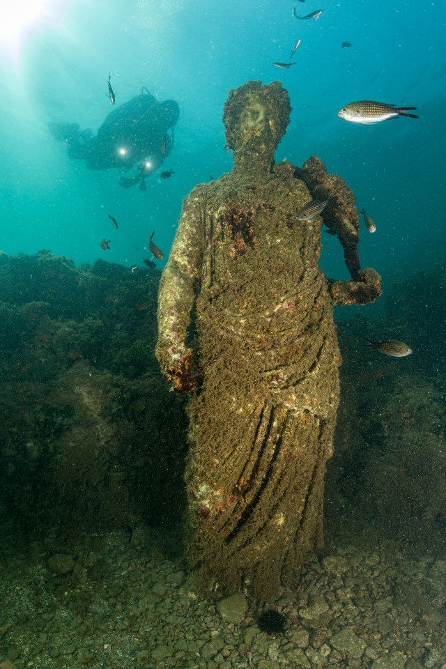 Moss-covered statues sit on the seabed in the lost city of Baia