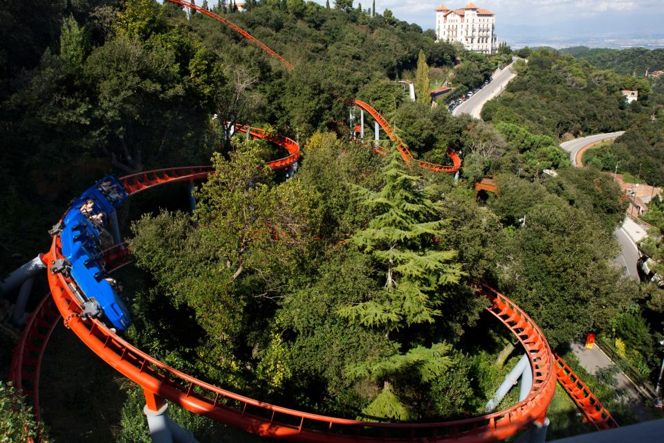 A red rollercoaster loops around tree tops in the theme park