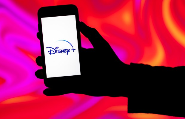 a hand is holding a phone with the disney plus logo on the screen