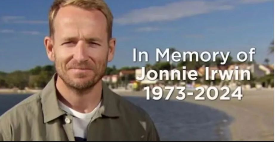 a man standing in front of a beach with the words in memory of jonnie irwin 1973-2024