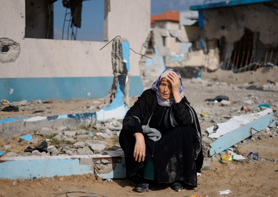 A woman rests next to a damaged building, as Palestinians arrive in Rafah after they were evacuated from Nasser hospital