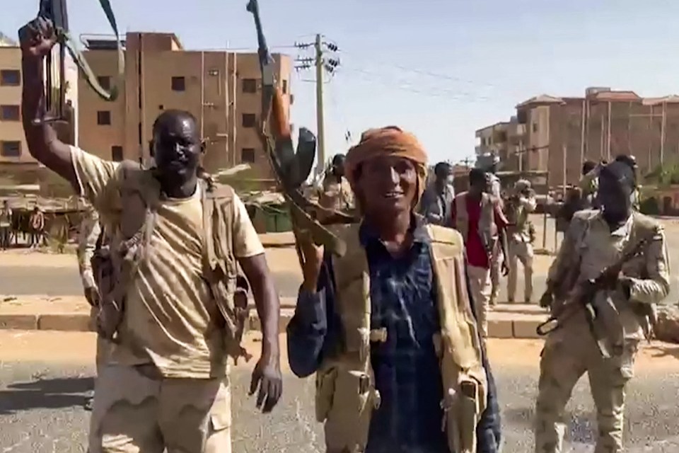 Rapid Support Forces fighters wave assault rifles as they cross a street in the East Nile district of greater Khartoum