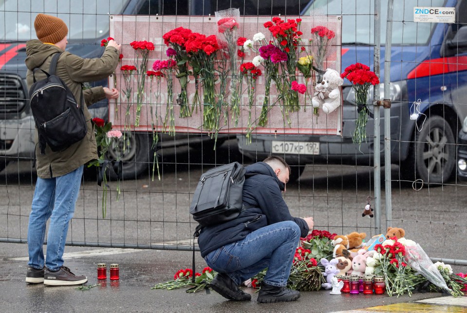 People bring flowers to the burned out venue as Russia mourns