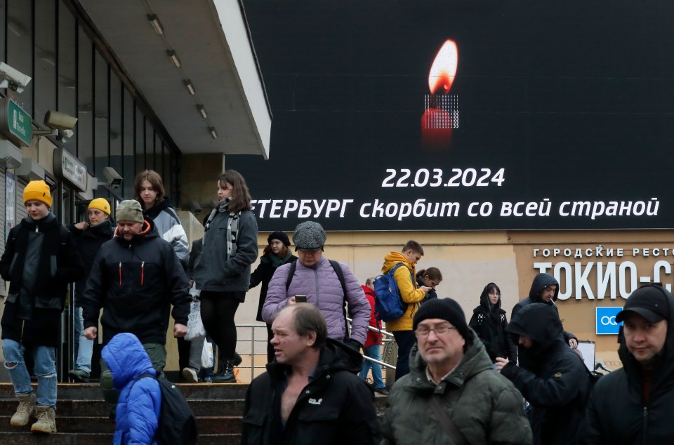 People walk past a huge digital billboard showing a burning candle in St Petersburg