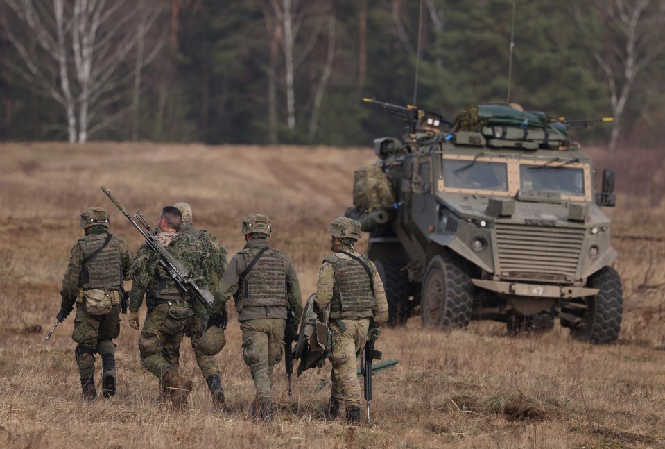 Spanish troops walk past a British mechanized infantry vehicle as in a NATO military exercise