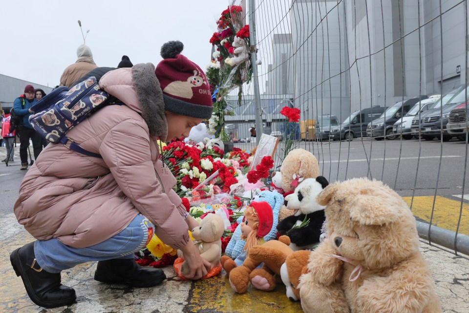 A child places a toy at the fence next to the Crocus City Hall