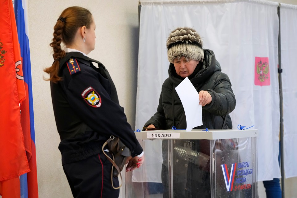 A security guard watches an elderly woman casts her ballot