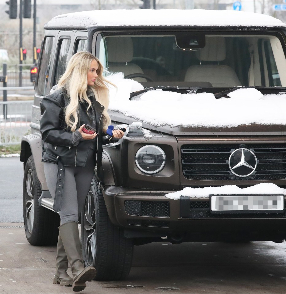 a woman standing in front of a mercedes with snow on the windshield