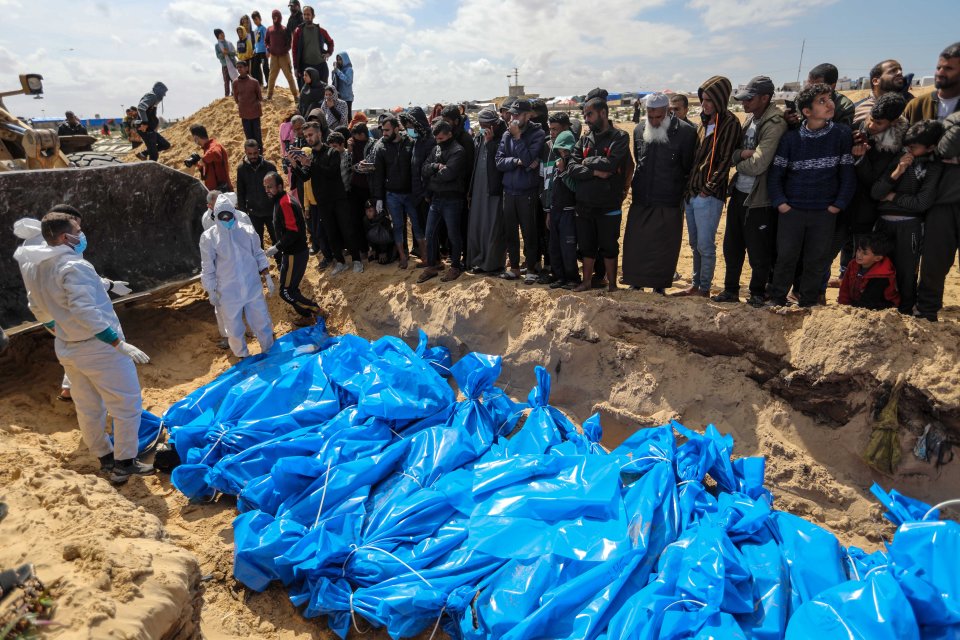 People surround a mass grave site in Gaza to watch as bodies get buried