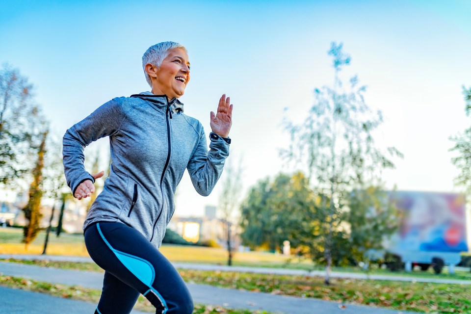 Joyful Senior Woman in Fitness Outfit Get Morning Running. Senior Woman Doing Her Jogging Outside at Public Park Trail. Mature Caucasian Woman Exercising at Park - Fitness, Sport, Training, Park and Lifestyle Concept.