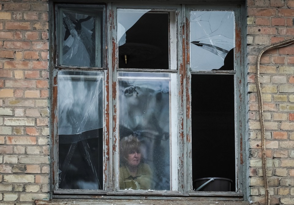 A local resident looks out of a window of her apartment building damaged during a Russian missile strike