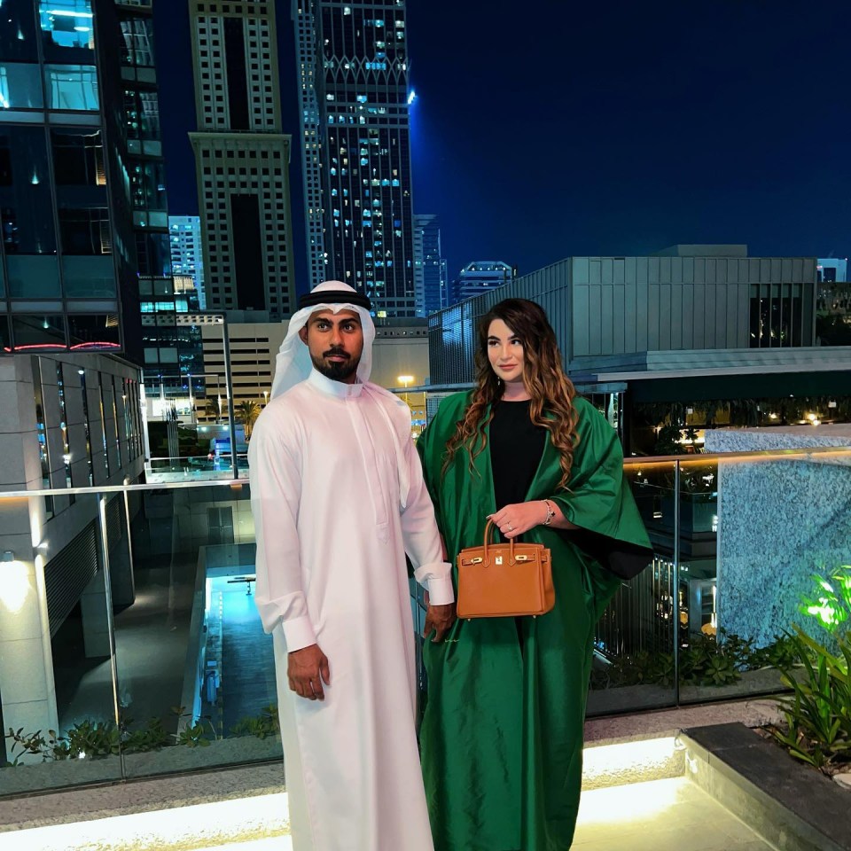 A man and woman stand holding hands in Dubai at night.