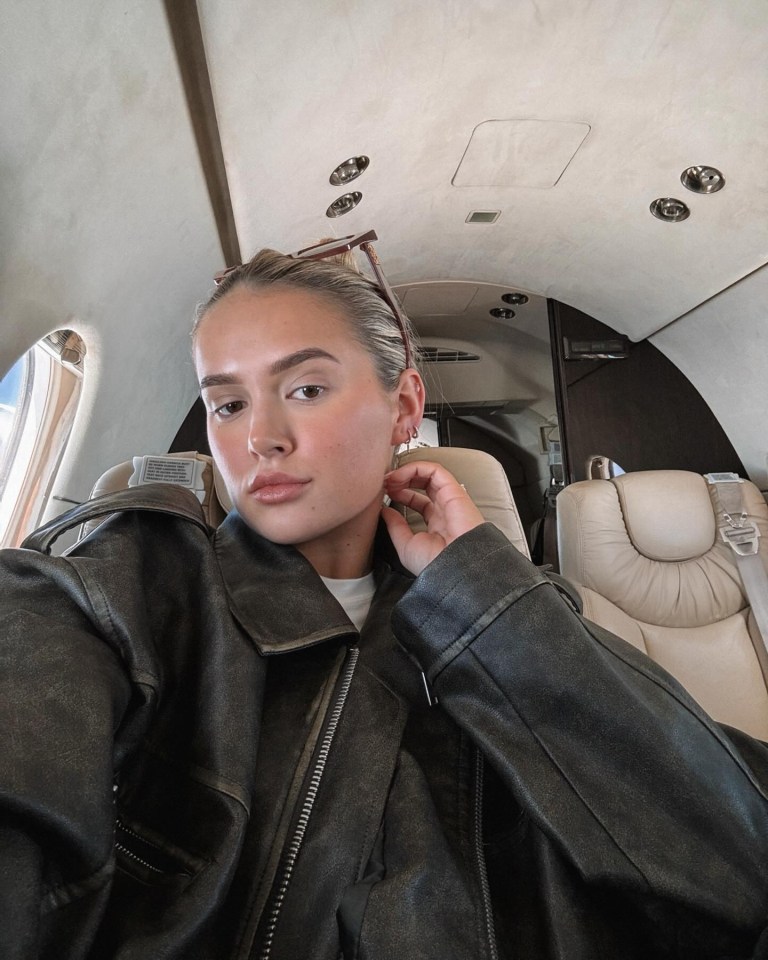 a woman in a leather jacket is sitting on a plane