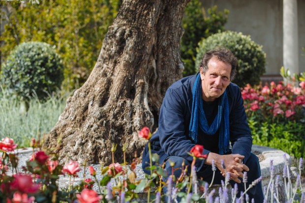 a man in a blue scarf sits next to a tree in a garden