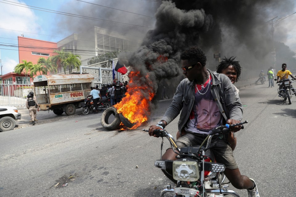 People drive past a burning blockade as chaos continued to spread across Haiti's capital