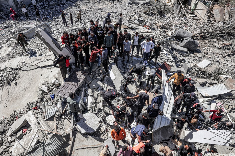 People wade through the debris of a building that collapsed in the Rafah refugee camp after an Israeli air strike