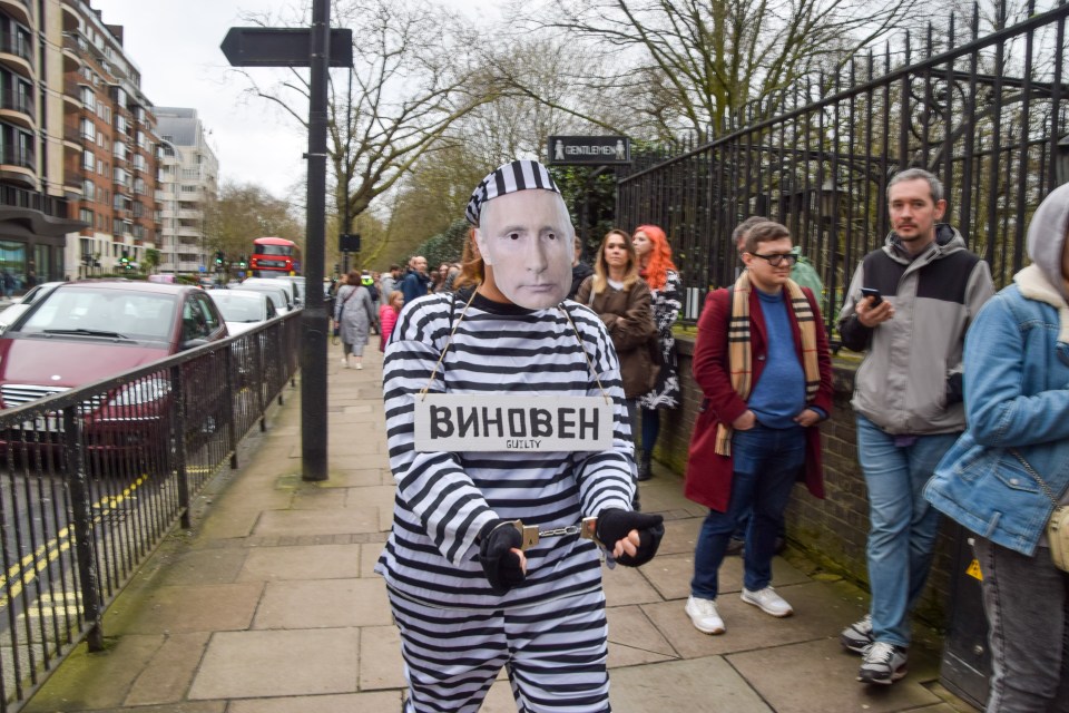 A protester dressed as Putin in prison stripes and handcuffs walks past Russians queuing to vote outside the embassy in London