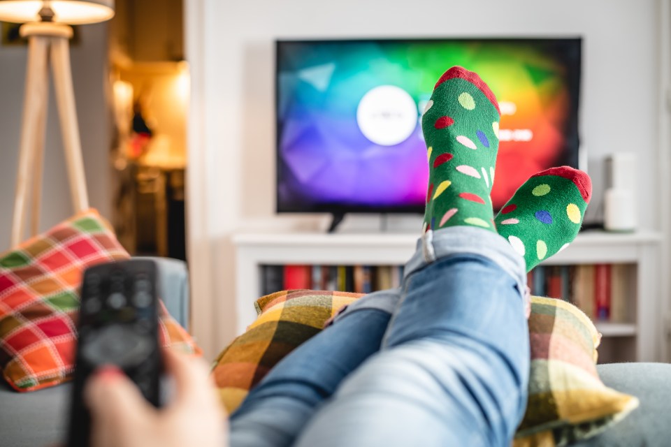 Woman holding remote controller in hand while watching tv at home