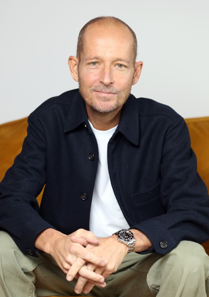 a man wearing a watch sits with his hands folded