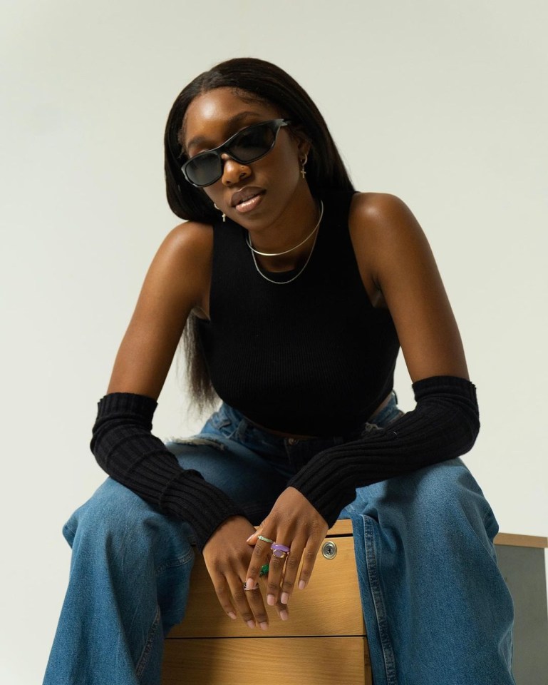 a woman wearing sunglasses and a black tank top sits on a wooden box