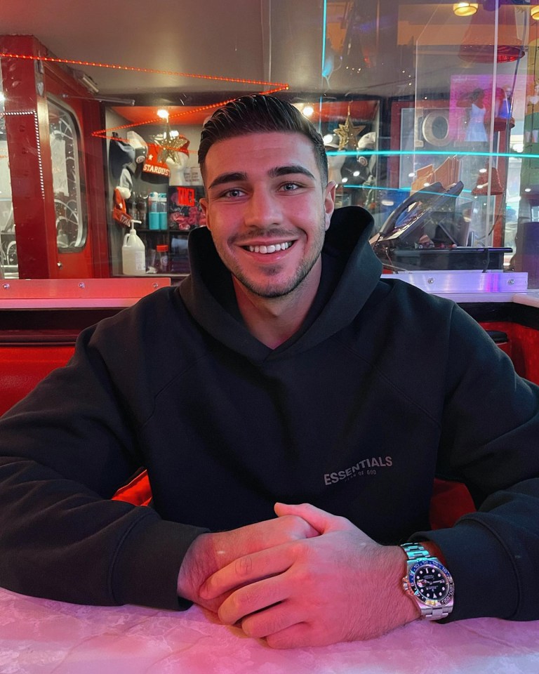 a man wearing a black essentials hoodie sits at a table