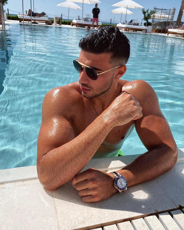 a shirtless man wearing sunglasses leans on the edge of a swimming pool