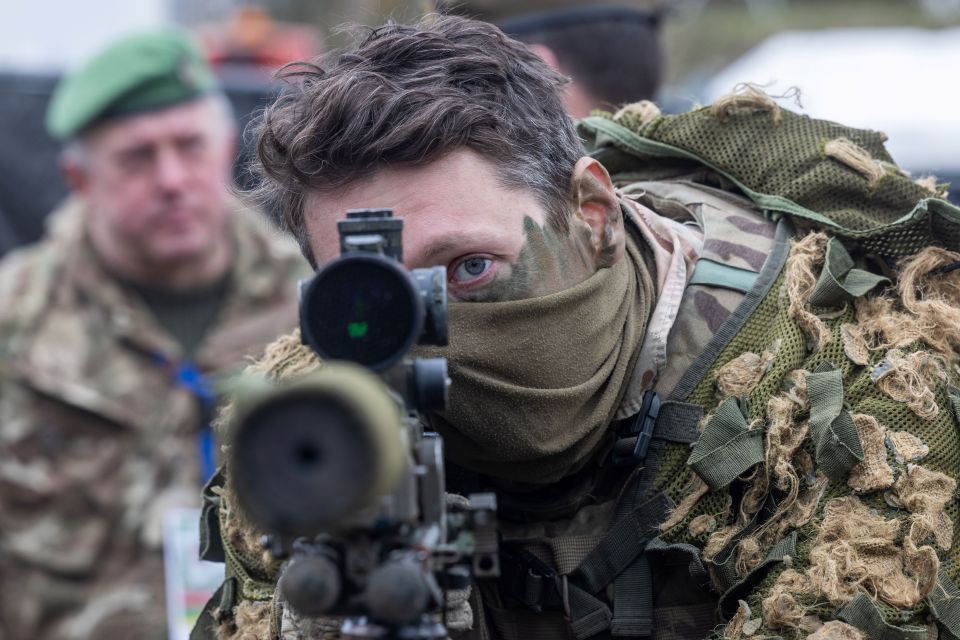 A British soldier looks into a telescopic sight as he holds his sniper rifle during the NATO DRAGON-24 military exercise