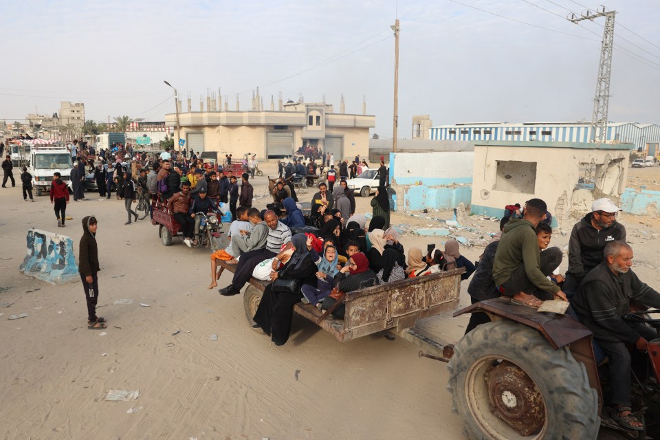 Families ride on the back of carriages next to damaged buildings