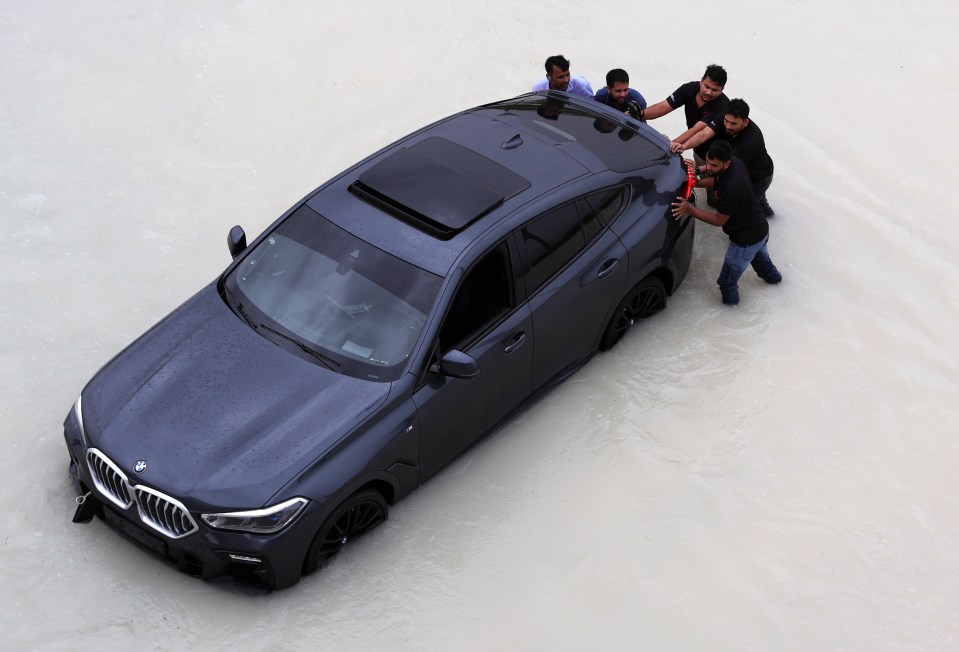 People push a car through floodwater amid heavy rainfall in Dubai