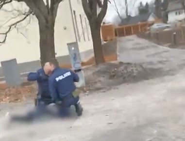 Two officers kneel next to a young person lying face down on the ground