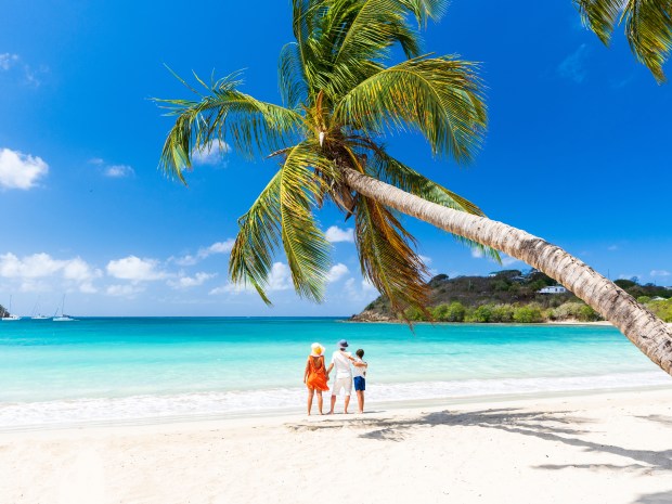 Two parents with one child hugging on palm fringed beach in summer, Antigua, Leeward Islands, Caribbean, West Indies