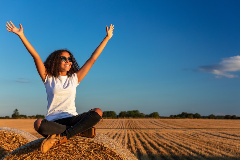 Beautiful, happy mixed race African American female girl child teenager young woman celebrating arms raised in sunshine wearing sunglasses and smiling with perfect teeth