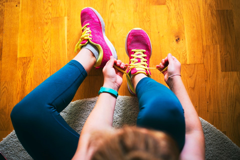 Young sporty woman with smart watch tying shoelaces