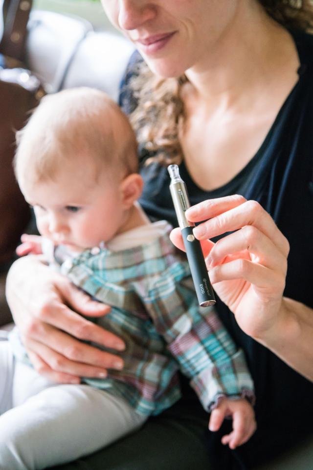 H21MXC Woman smoking electronic cigarette beside a baby.