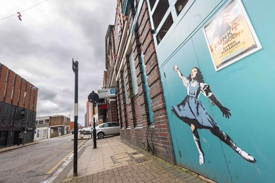 Dorothy from the Wizard of Oz reaches for a pair of ruby red slippers hanging from a nearby electric cable