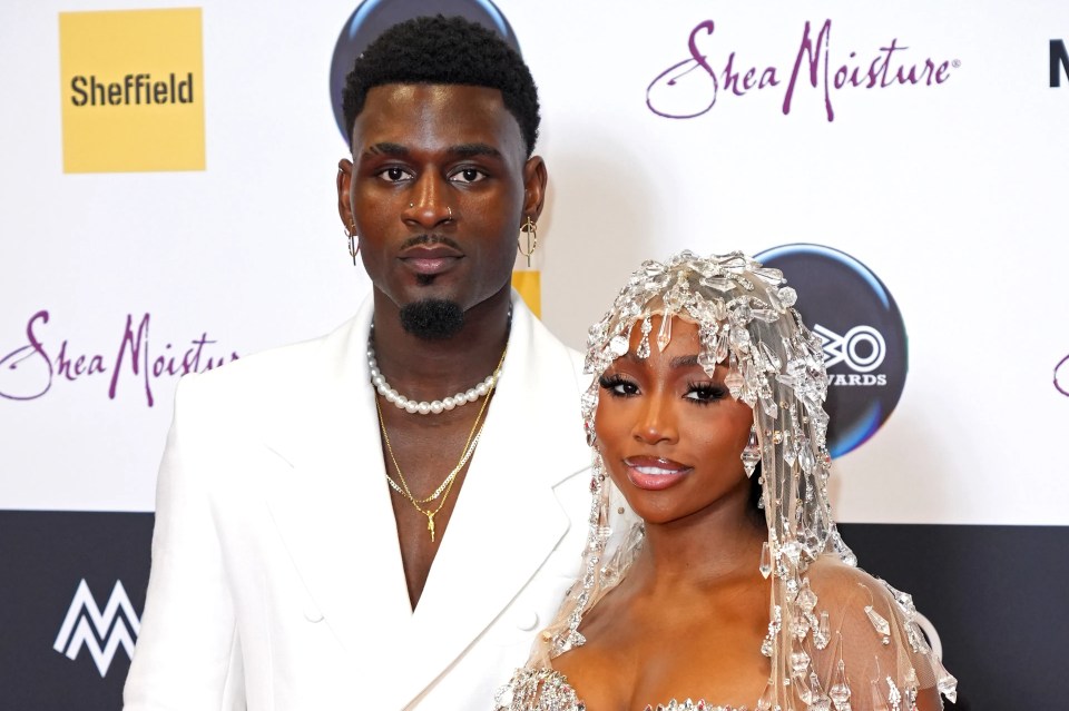 a man and a woman are standing on a red carpet in front of a shea moisture sign