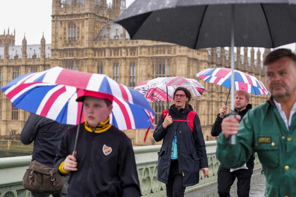 Pedestrians carrying umbrellas cross Westminster Bridge, in London, at the weekend