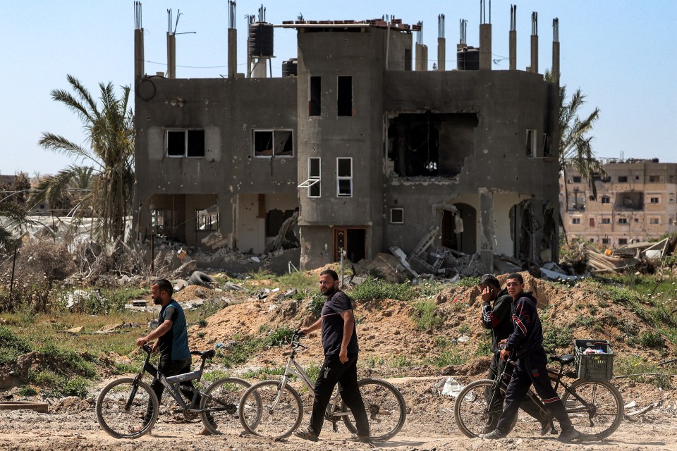 Men walk with bicycles along a heavily damaged road