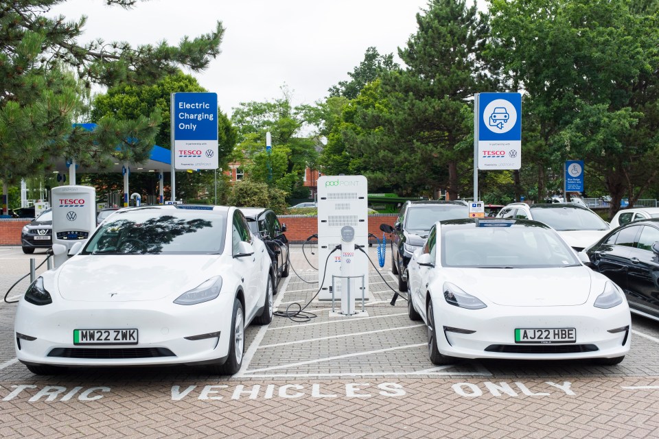 Two white Tesla EV cars refuel at an electric car charging station in a Tesco car park in Poole