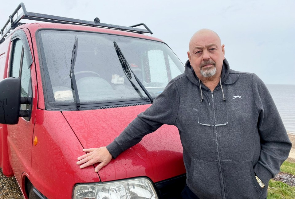 a man wearing a slazenger sweatshirt stands in front of a red van