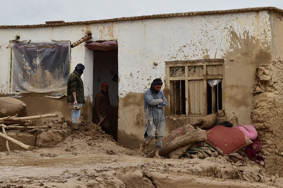 Afghan men clear debris and mud from a damaged house following a flash flood