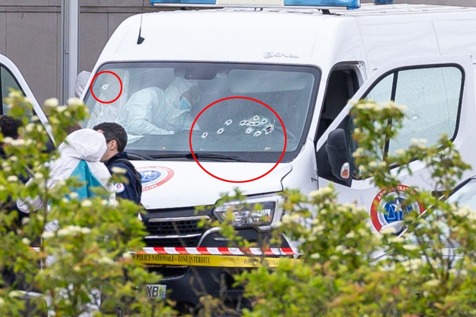 A spray of bullet holes in the windshield of a police van at the scene of the attack this morning