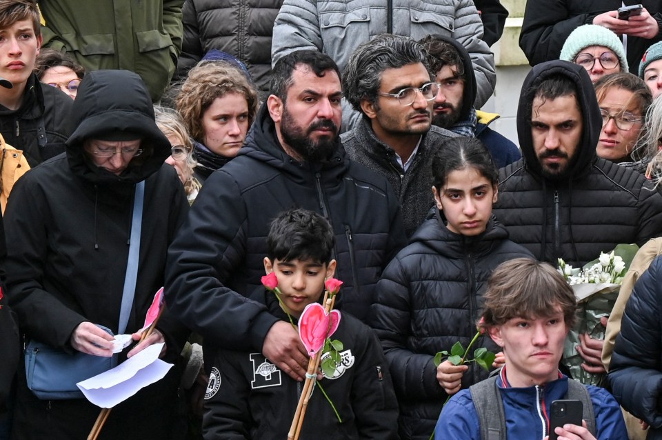 Ahmed Alhashimi (C) Iraqi father of Sara, a seven-year-old girl who died while trying to cross the Channel with her father and two of her siblings Hussam (C-L) and Rahaf (C-R) stand next to local residents and migrants to pay tribute to migrants who died trying to cross the channel in Wimereux, northern France, on May 2, 2024. Five people including a seven-year-old Iraqi girl (Sara) died after a boat carrying migrants heading to Britain sank in the Channel on April 23, 2024. (Photo by Bernard BARRON / AFP) (Photo by BERNARD BARRON/AFP via Getty Images)