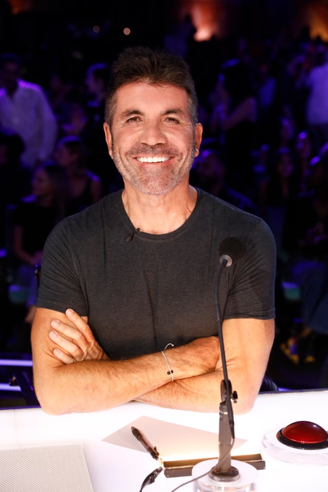 a man with his arms crossed smiles in front of a microphone