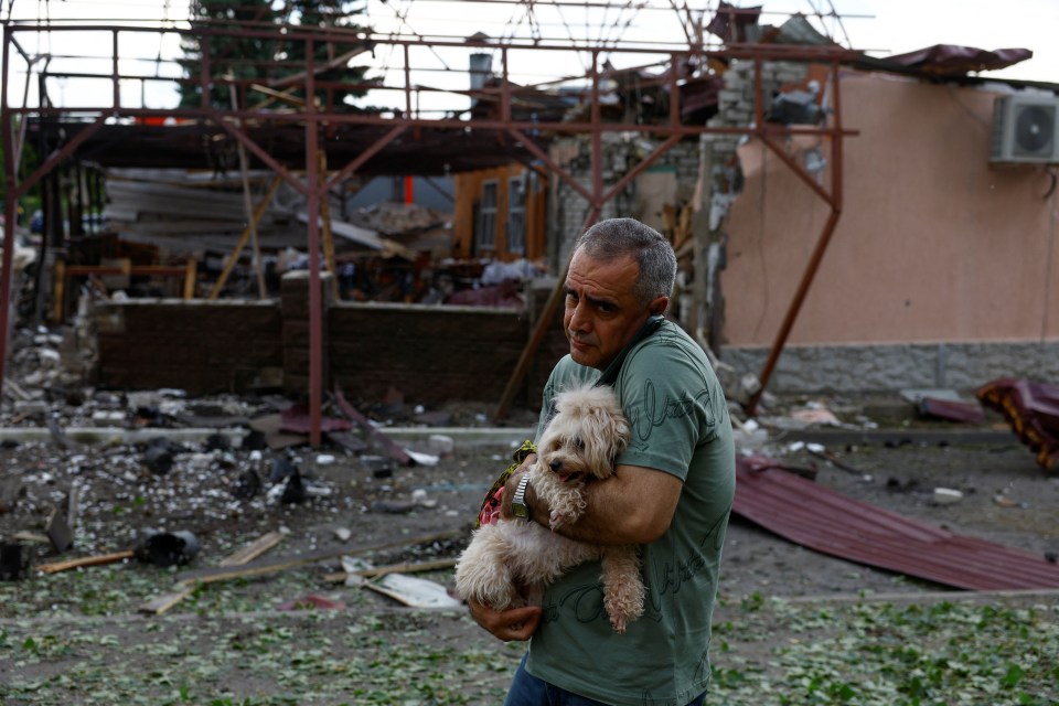 A man holds a dog next to his cafe heavily damaged by a Russian air strike in Kharkiv