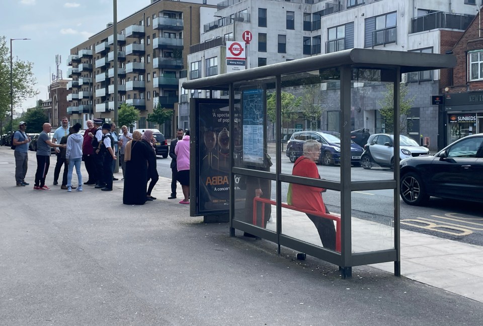 Police speak to members of the public at a bus stop near to the scene