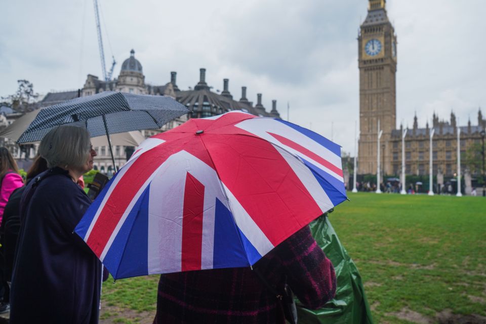 A tourist in Parliament Square shelters under an umbrella during showers today