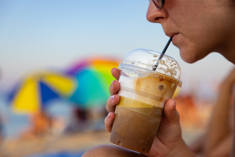 a woman drinking from a plastic cup that says ' iced coffee ' on it