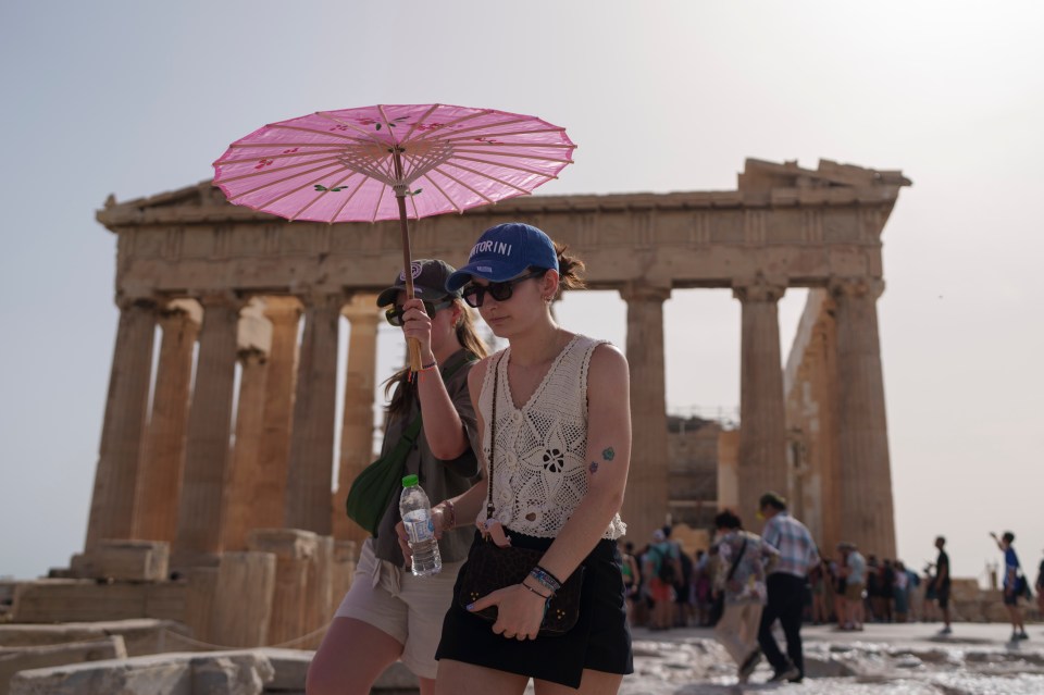 Tourists walking outside the Parthenon at the ancient Acropolis Athens with an umbrella after the attraction was closed off due to the weather