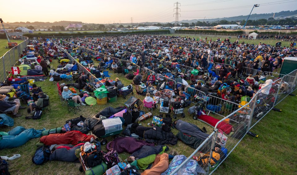 a large crowd of people are gathered in a field behind a fence